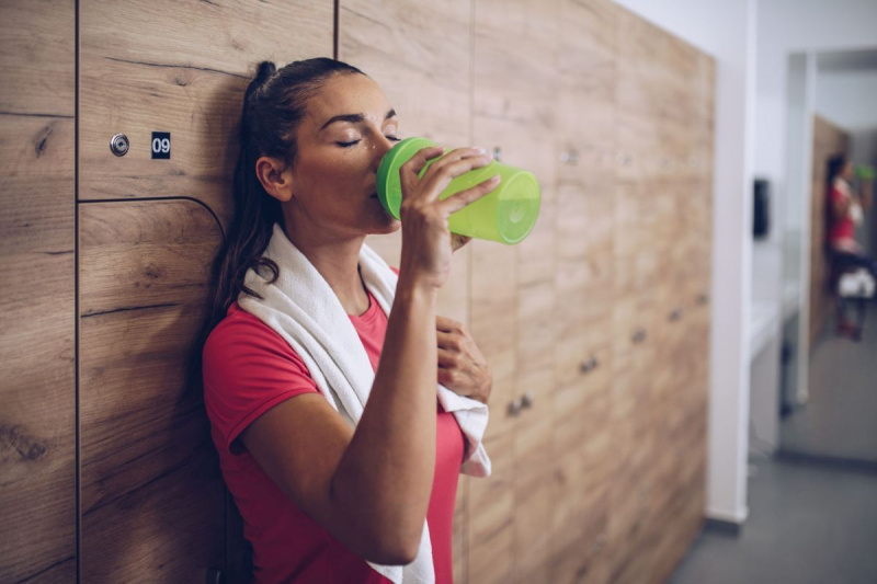 Mulher exausta bebendo água no vestiário após o treinamento esportivo.