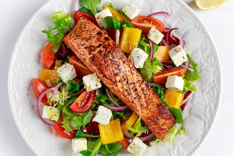 फ्राइड सैल्मन स्टेक ताजी सब्जियों के सलाद, फेटा चीज के साथ। स्वस्थ भोजन की अवधारणा।