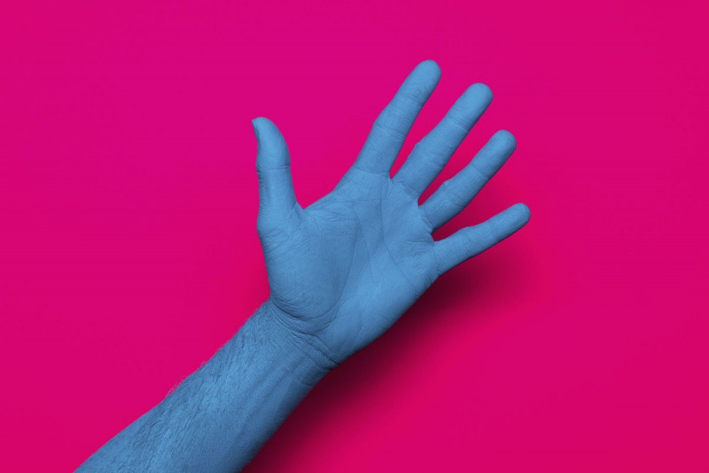 Close de uma mão pintada de azul contra um fundo rosa