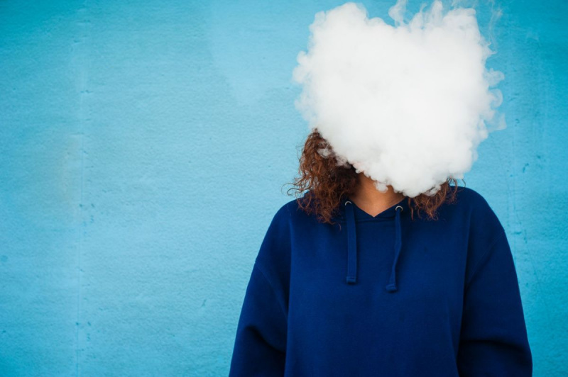 Mulher jovem com a cabeça em uma nuvem de fumaça de vapor