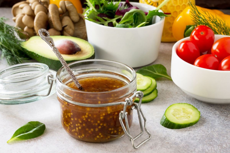Superpotraviny a domáci šalátový dresing vinaigrette s horčicou, medom, balzamikovým octom a olivovým olejom na pozadí kameňa alebo bridlice.