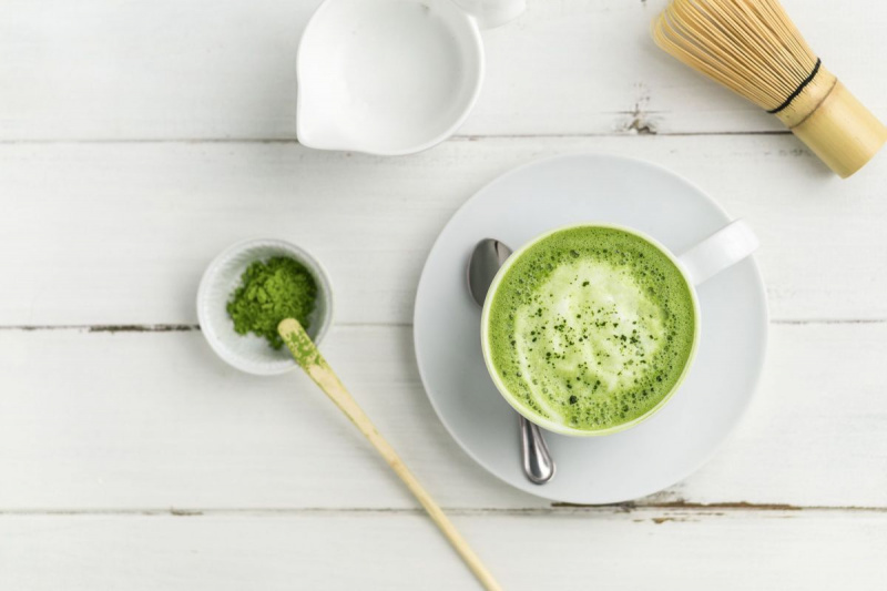 Xícara de café com leite matcha de chá verde em fundo branco da vista plana de cima.