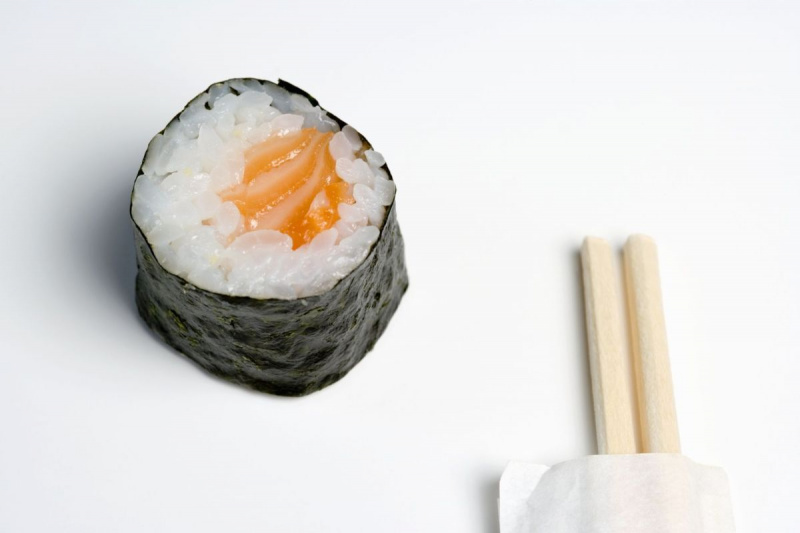 Pauzinhos de madeira ao lado de um pedaço de sushi de salmão