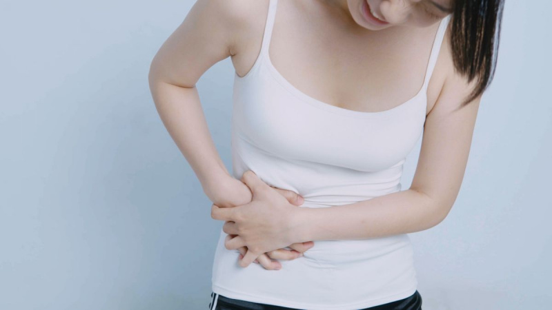 Seção mediana de uma mulher com dor de estômago em pé contra um fundo branco