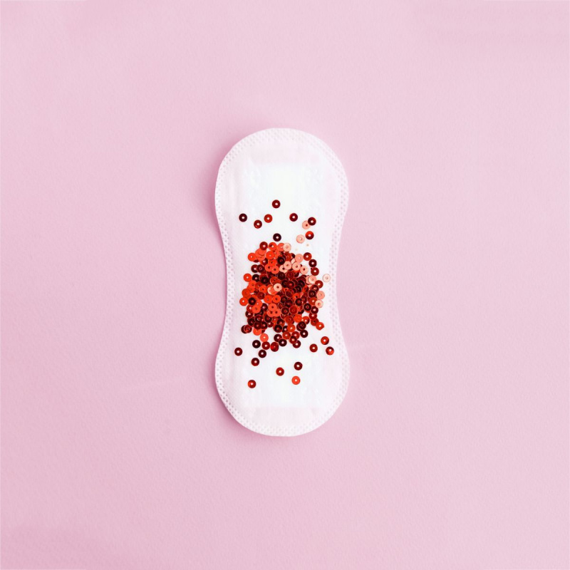 Menstruationspude med rødt glitter på pastel baggrund