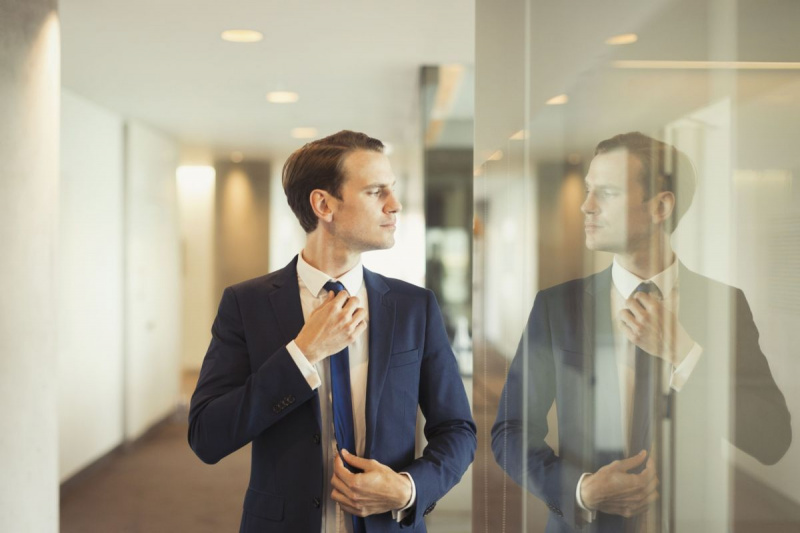 Уверен бизнесмен регулира вратовръзката в офис коридора
