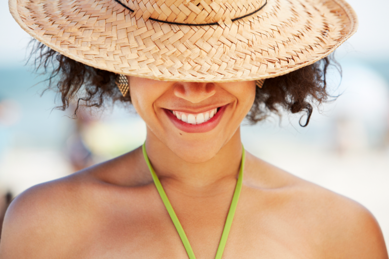 цветна жена, носеща слънчева шапка над очите, докато се усмихва