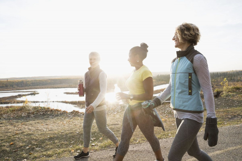 Жени, ходещи упражнения по слънчева пътека в есенния парк