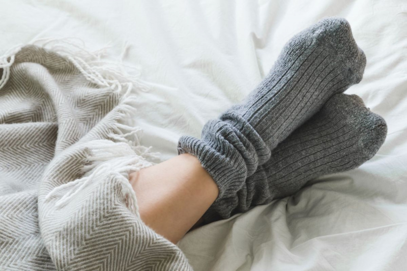 Краката са кръстосани със сиви чорапи на леглото под одеялото