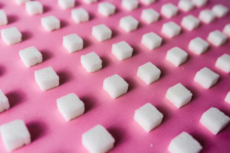 Крупни план коцкица шећера поређаних на розе столу