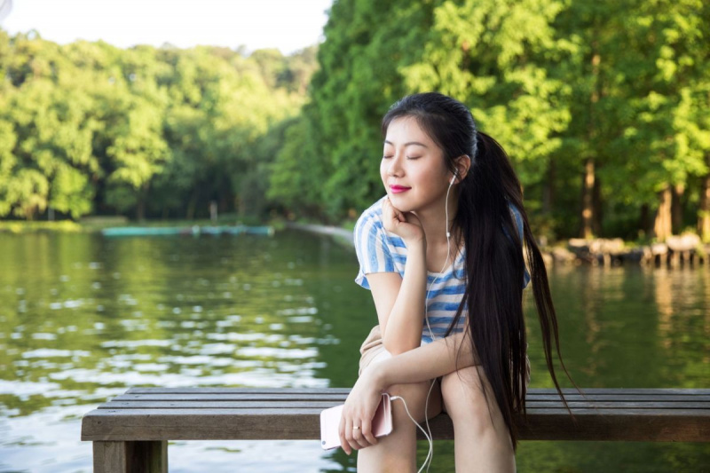 Jauna moteris sėdi prieplaukoje prie ežero ir šypsosi užsimerkusi